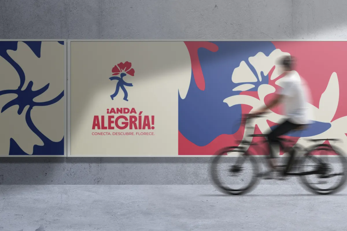 Mural de ¡Anda, Alegría! con flores en rojo, azul y crema en un muro urbano; un ciclista pasa frente a él.