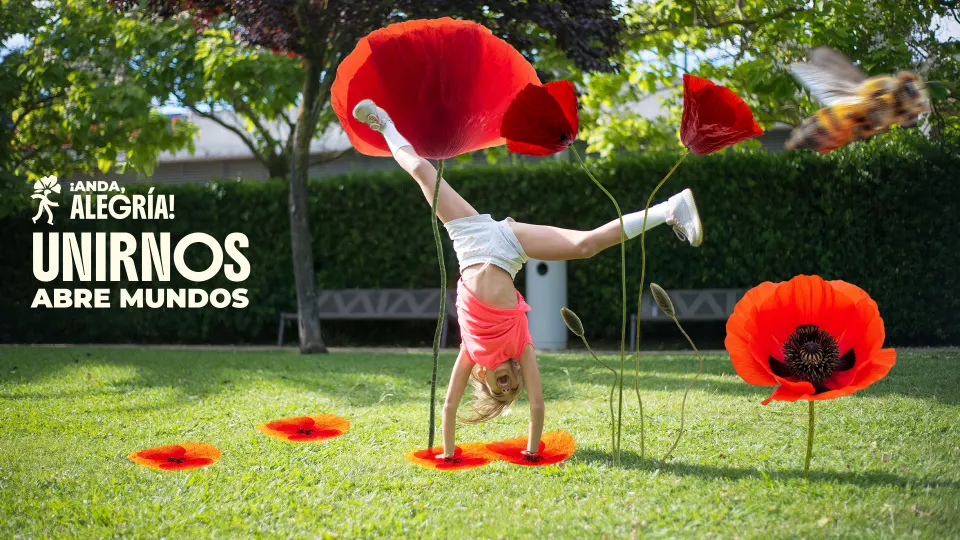 Niña haciendo la rueda en un parque entre amapolas gigantes, junto al lema “Unirnos abre mundos”.
